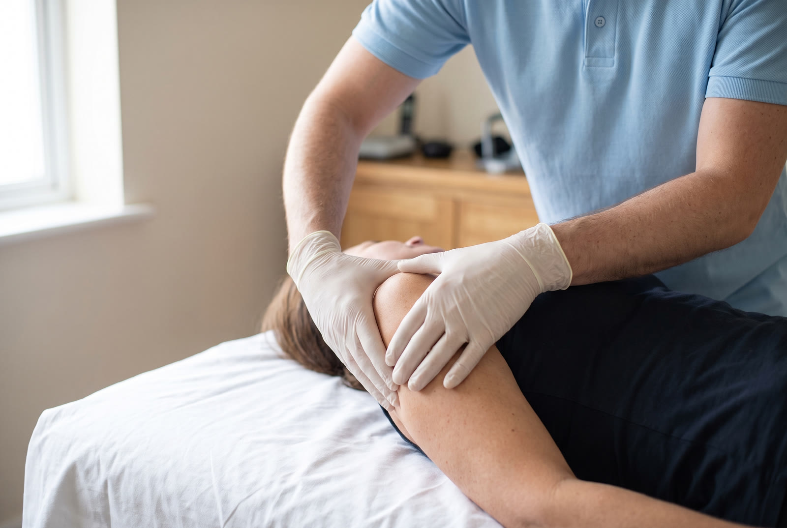 Physiotherapeut mobilisiert vorsichtig die Schulter einer Patientin auf der Behandlungsliege